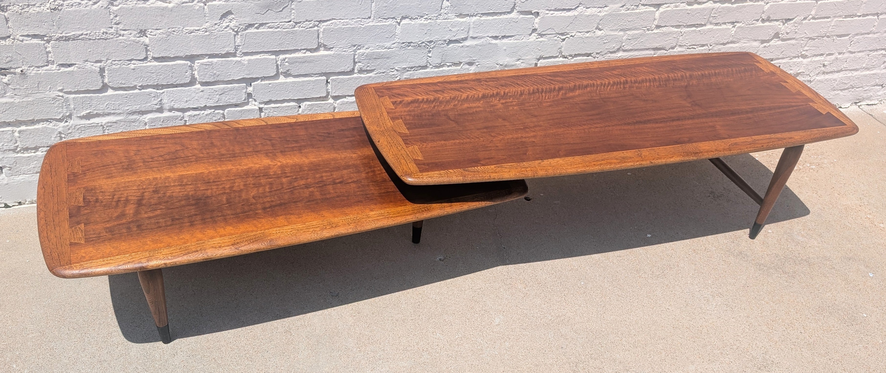 Wooden coffee table with a reflective surface on a concrete floor against a white brick wall.